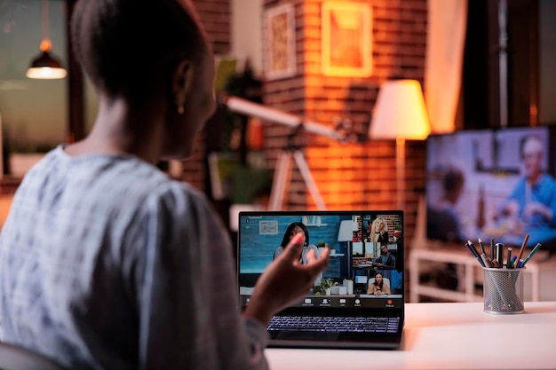 Teleconferencia con compañeros de trabajo, lluvia de ideas en equipo remoto sobre reuniones de negocios en línea. Mujer de negocios afroamericana charlando con colegas en videoconferencia usando laptop, vista trasera