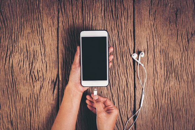 Foto gratuita teléfono de carga de la mano de la visión superior en el fondo de madera