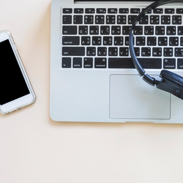 Teléfono celular y auriculares en el teclado de la computadora portátil sobre el fondo coloreado