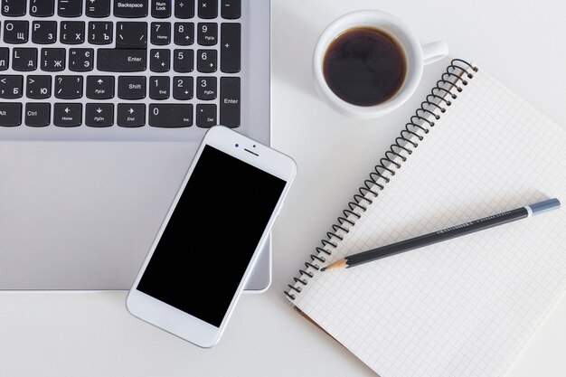 Teléfono celular en la computadora portátil con una taza de café y un lápiz sobre el portátil