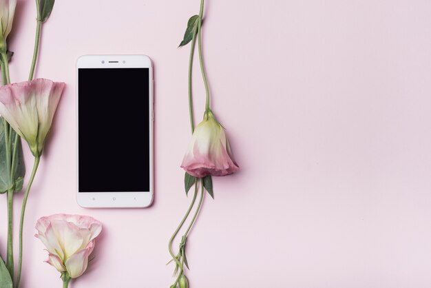 Teléfono celular con flores eustoma contra fondo rosa