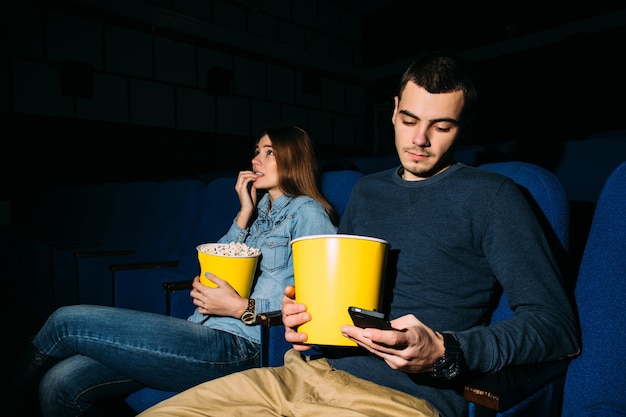 Teléfono inteligente en el cine. Hombre que usa el teléfono inteligente mientras ve la película en el cine.