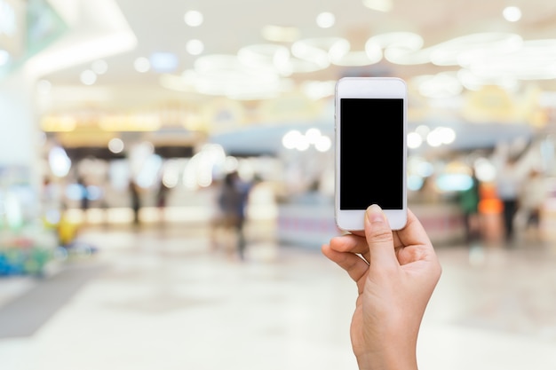 Teléfono inteligente con pantalla en blanco en la mano en borrosa en el centro comercial de fondo, compras en línea concepto, compras por teléfono inteligente