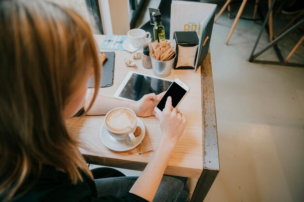 Teléfono inteligente sin rostro de navegación de mujer joven en café