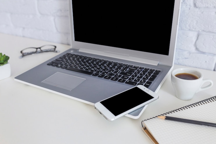 Foto gratuito teléfono móvil en la computadora portátil con la taza de café en el escritorio blanco