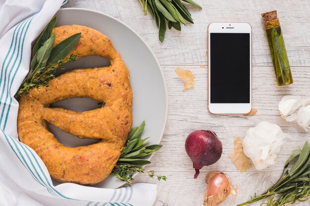 Foto gratuita teléfono móvil; ingredientes y pan oval al horno en plato contra fondo de madera