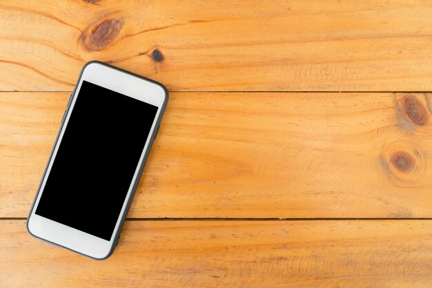 Teléfono móvil con pantalla en blanco sobre fondo de madera de mesa. Vista superior con espacio de copia.