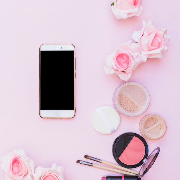 Foto gratuita teléfono móvil; productos cosméticos y flores sobre fondo rosa sobre fondo rosa