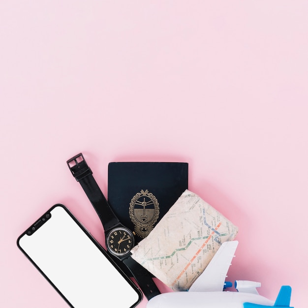 Foto gratuita teléfono móvil; reloj de pulsera; pasaporte; mapa y avión en miniatura sobre fondo rosa