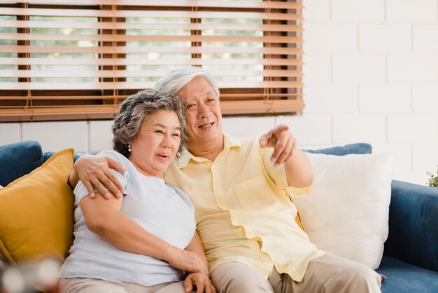 La televisión de observación de los pares mayores asiáticos en la sala de estar en casa, pareja dulce disfruta del momento del amor mientras que miente en el sofá cuando está relajado en casa.