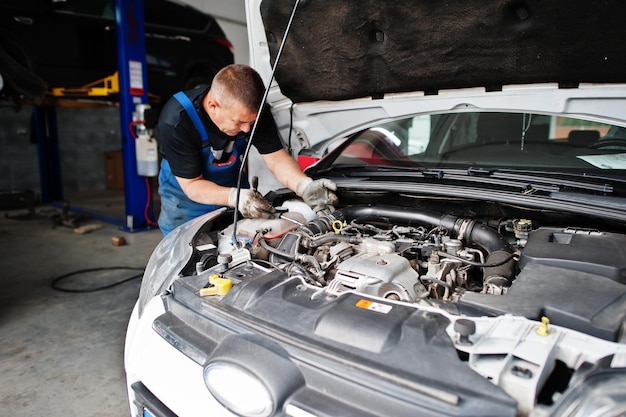 Tema de reparación y mantenimiento de automóviles Mecánico en uniforme trabajando en motor de control de servicio automático