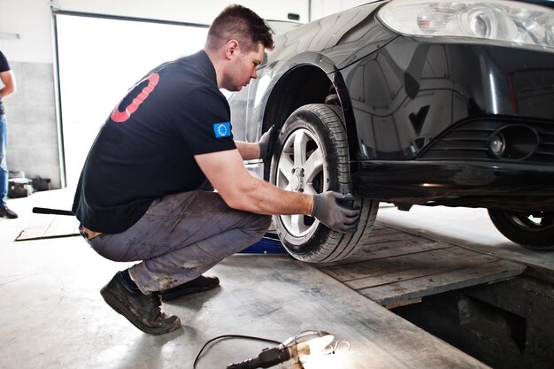 Tema de reparación y mantenimiento de automóviles Mecánico en uniforme trabajando en servicio automático revisando neumáticos
