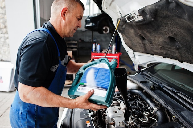 Tema de reparación y mantenimiento de automóviles Mecánico en uniforme trabajando en servicio automático vertiendo aceite de motor nuevo