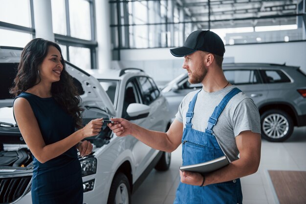 Ten mas cuidado la próxima vez. Mujer en el salón del automóvil con empleado en uniforme azul tomando su auto reparado