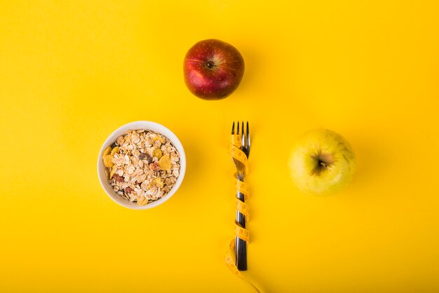 Tenedor en cinta métrica entre manzanas y tazón de copos.