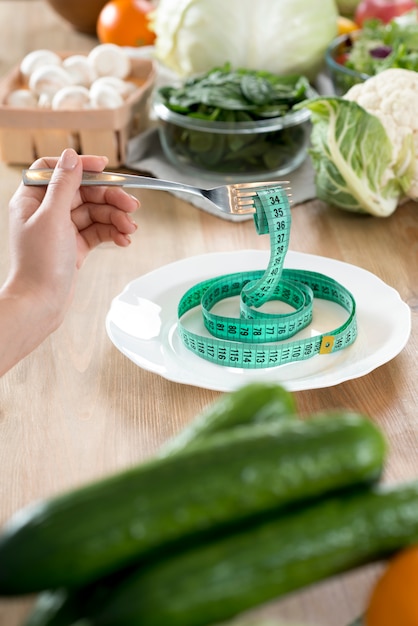 Tenedor de la mano de la mujer con cinta métrica verde en un plato blanco sobre cocina mostrador