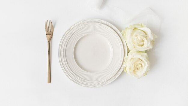Tenedor; plato de cerámica; Rosas y cinta de raso sobre fondo blanco.