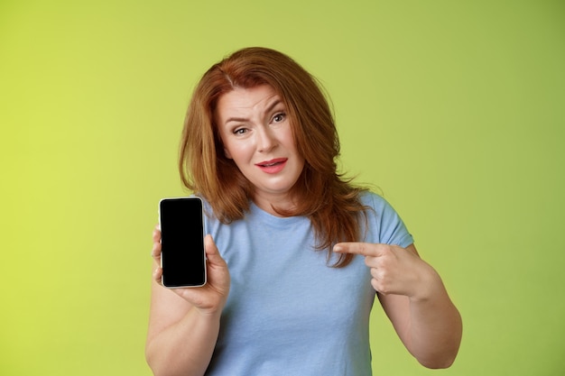 Tener algo que decir cuestionó seriamente mirada disgustada pelirroja madura madre actuando enojada sostener el teléfono inteligente señalando la pantalla del teléfono móvil en blanco exigir respuestas encontradas hija fotos de redes sociales