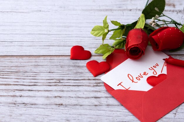 Tenga en cuenta que dice "Te amo" dentro de un sobre con corazones y rosas en la mesa de madera