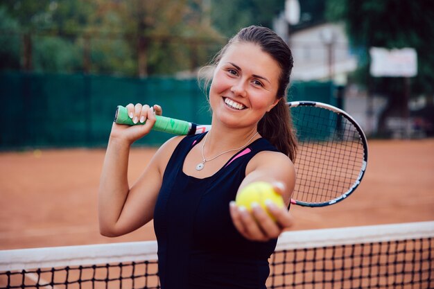 Tenista. Atractiva mujer activa de pie en la cancha con raqueta de tenis y pelota