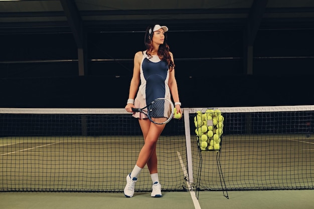 Tenista morena sexy posando en una cancha de tenis cubierta.