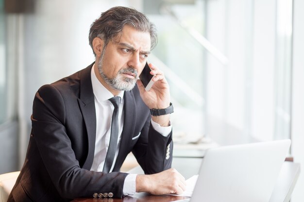 Tensed hombre de negocios hablando por teléfono en el escritorio