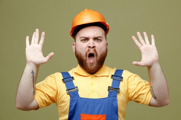 Tenso extendiendo las manos joven constructor hombre en uniforme aislado sobre fondo verde