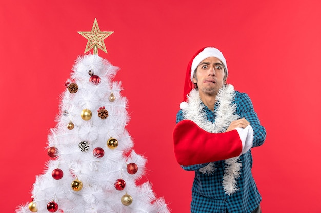 Tenso joven con sombrero de santa claus en una camisa azul a rayas y poniendo algo