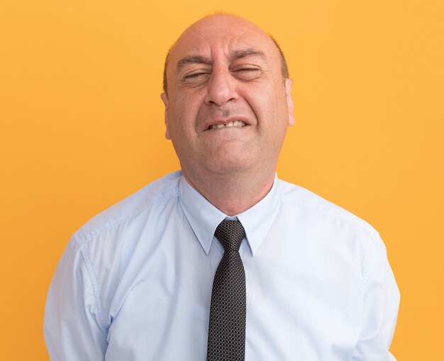 Tenso con los ojos cerrados hombre de mediana edad vestido con camiseta blanca con corbata aislado en la pared naranja