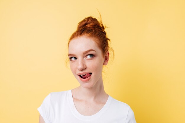 Tentadora mujer de jengibre en camiseta lamiendo labios y mirando a otro lado