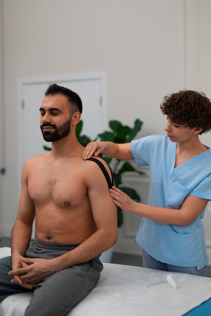 Terapeuta femenina en el centro de rehabilitación poniendo soporte para el hombro en el hombre