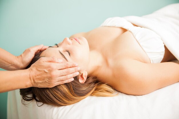 Terapeuta femenina equilibrando la energía de un cliente durante una sesión de reiki en un spa de salud. Ambas manos en la sien