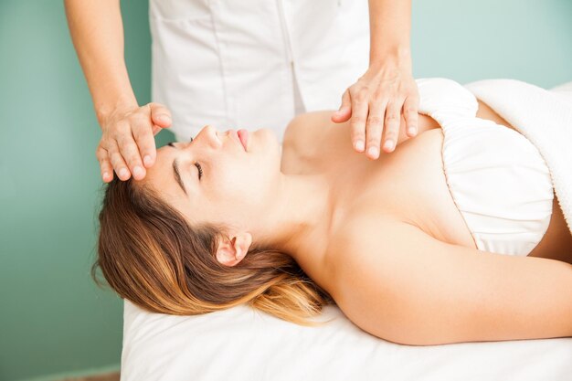 Terapeuta femenina transfiriendo buenas vibraciones y energía a un cliente en un spa de salud. Una mano sobre la cabeza y otra sobre el pecho.