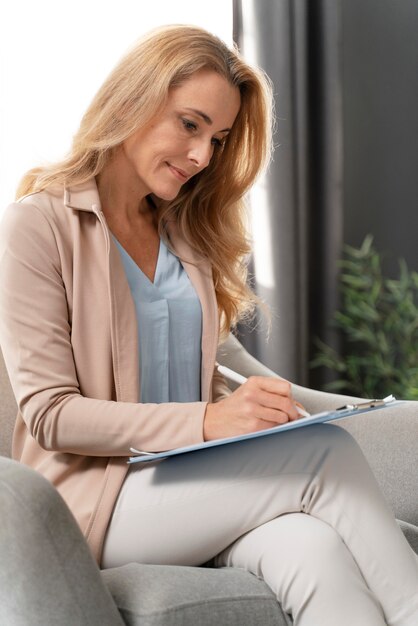 Terapeuta de mujer de tiro medio escribiendo en portapapeles