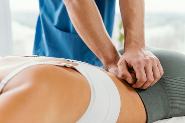 Terapeuta osteopático masculino comprobando la columna lumbar del paciente femenino