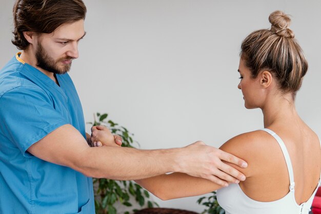 Terapeuta osteopático masculino comprobando el movimiento del hombro del paciente femenino