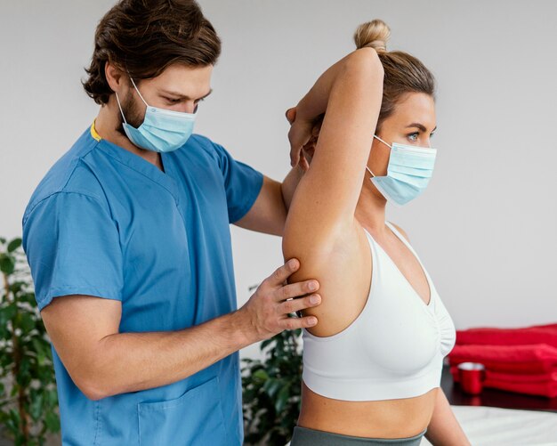 Terapeuta osteopático masculino con máscara médica comprobando la articulación del hombro del paciente femenino