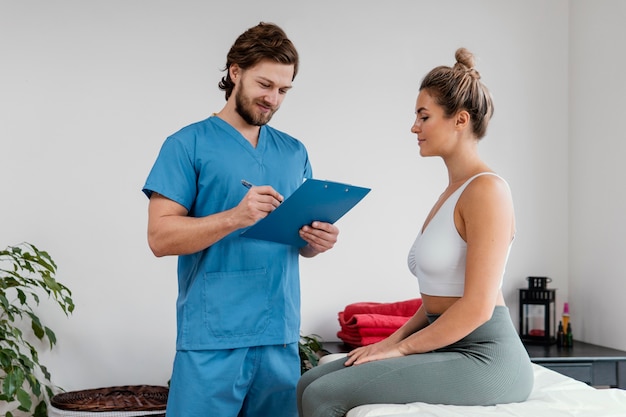 Terapeuta osteopático masculino con portapapeles de firma paciente femenino en la clínica