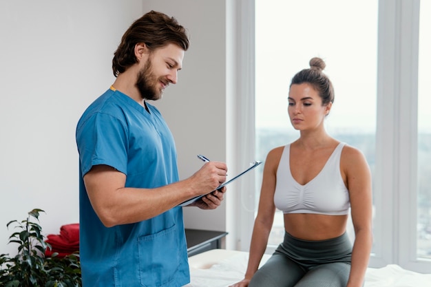 Terapeuta osteopático masculino con portapapeles firma paciente femenino en la oficina