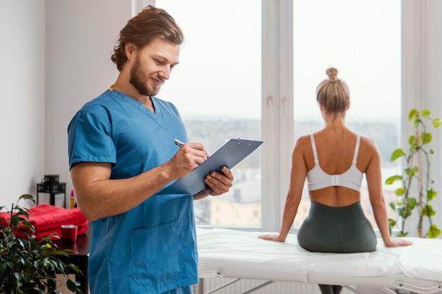 Foto gratuita terapeuta osteopático masculino con portapapeles y paciente en la oficina