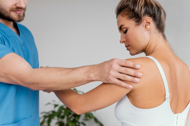 Terapeuta osteopático masculino que controla el dolor de hombro del paciente femenino