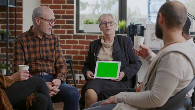 Terapeuta sosteniendo la tableta con pantalla verde horizontal en una reunión con personas. Psiquiatra mujer mostrando clave de croma y plantilla de maqueta aislada en exhibición para pacientes con adicción.