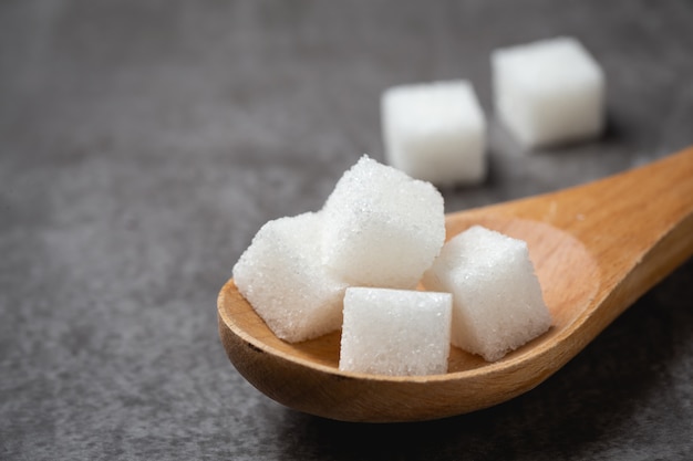 Terrón de azúcar blanco en la cuchara de madera sobre la mesa.