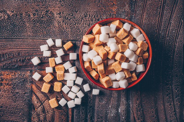 Terrones de azúcar blanco y marrón en un tazón de naranja sobre una mesa de madera oscura. vista superior.