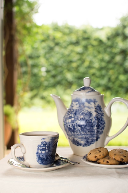 Tetera de porcelana y tazas de té con galletas en forma de ballena en la mesa al aire libre