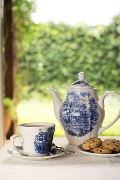 Tetera de porcelana y tazas de té con galletas en forma de ballena en la mesa al aire libre