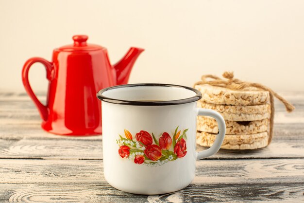 Una tetera roja vista frontal con taza de café y galletas en la mesa rústica gris beber color café