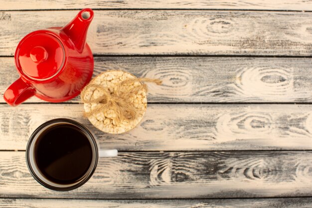 Una tetera roja de vista superior con una taza de café y galletas en el escritorio rústico gris beber color café