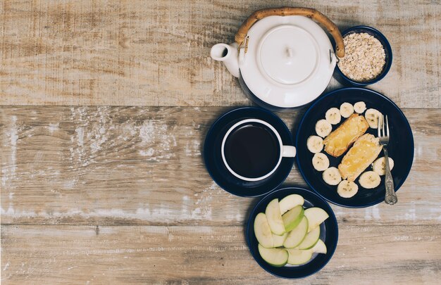 Tetera; Taza de café y desayuno saludable sobre fondo con textura de madera