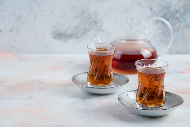 Tetera y vaso de té de dos vasos sobre superficie blanca